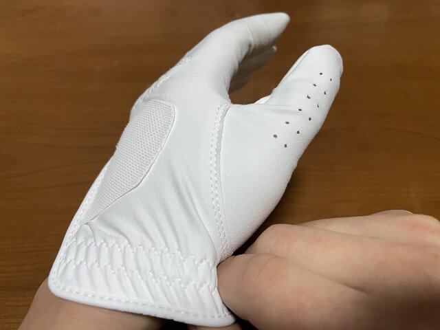 ［ゴルフグローブの着け方］親指側の裾の部分をずらして親指を8割方入れる