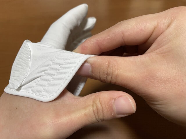 ［ゴルフグローブの外し方］裾と親指の先にある生地をつまみながら親指を抜く